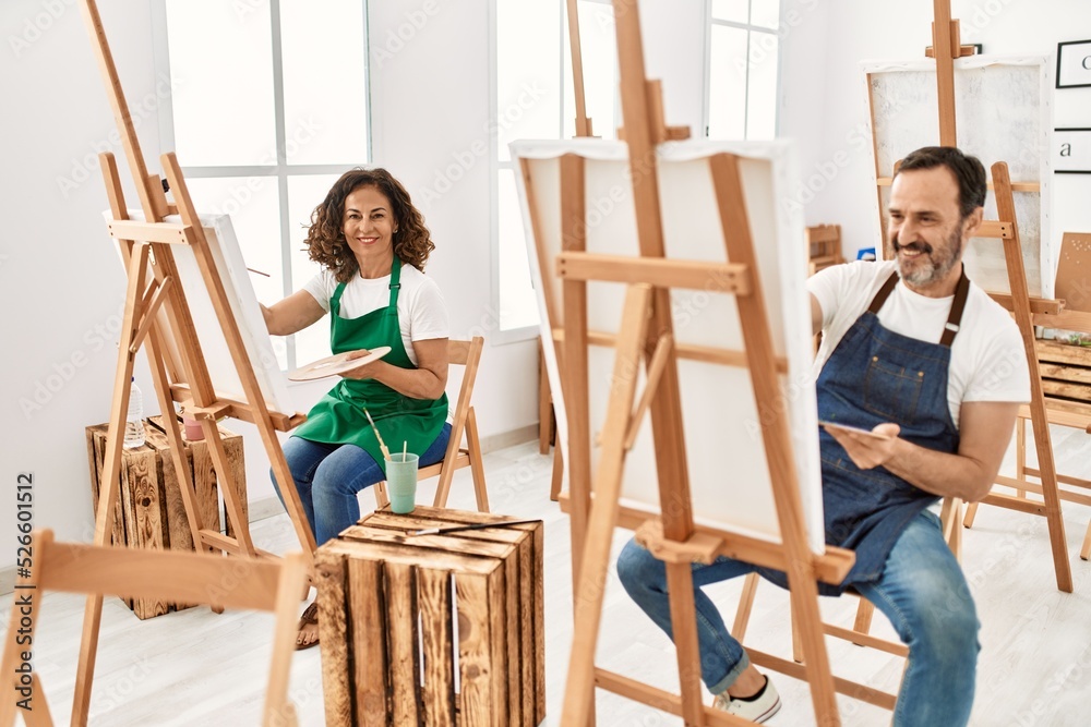 Two middle age student smiling happy painting at art studio.