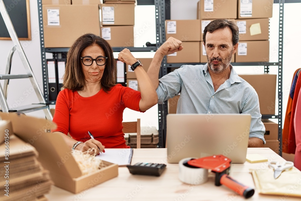 Middle age couple working at small business ecommerce strong person showing arm muscle, confident and proud of power Middle age couple working at small business ecommerce strong person showing arm muscle, confident and proud of power
