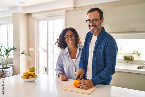 Middle age hispanic couple smiling confident cutting orange at kitchen