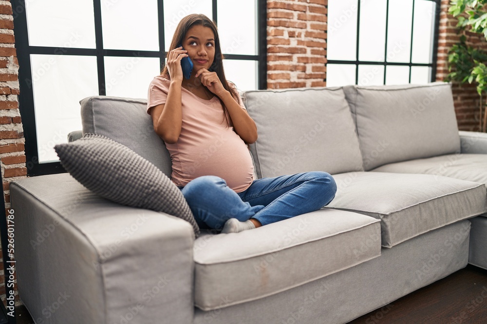 Obraz premium Young pregnant woman having conversation speaking on the smartphone serious face thinking about question with hand on chin, thoughtful about confusing idea