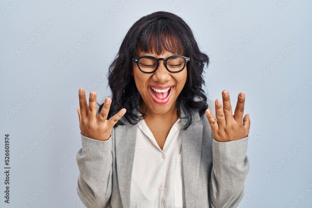 Hispanic woman standing over isolated background celebrating mad and crazy for success with arms raised and closed eyes screaming excited. winner concept