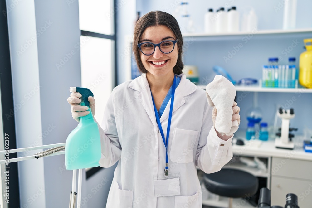 Young hispanic woman wearing scientist uniform cleaning using sanitizer gel at laboratory Young hispanic woman wearing scientist uniform cleaning using sanitizer gel at laboratory