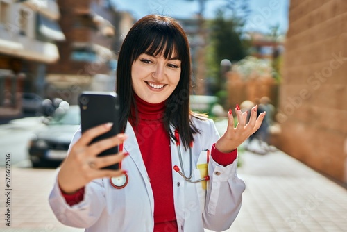 Young brunette woman wearing doctor uniform doing videocall with smartphone at the city