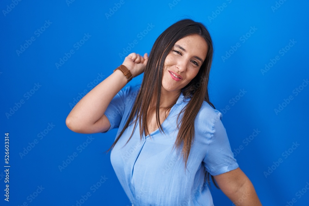 Fototapeta premium Young brunette woman standing over blue background dancing happy and cheerful, smiling moving casual and confident listening to music