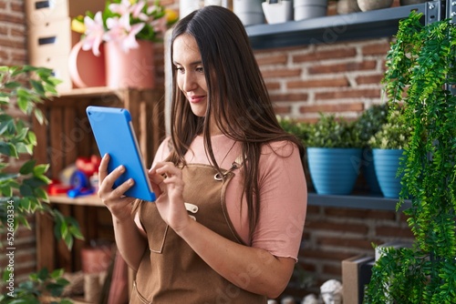 Young beautiful hispanic woman florist smiling confident using touchpad at flower shop