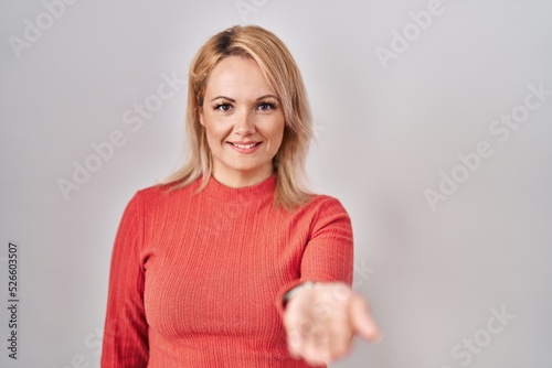 Blonde woman standing over isolated background smiling cheerful offering palm hand giving assistance and acceptance.