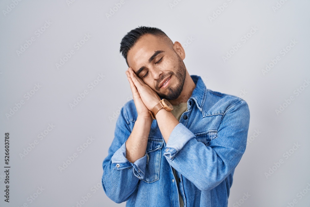 Young hispanic man standing over isolated background sleeping tired dreaming and posing with hands together while smiling with closed eyes. Young hispanic man standing over isolated background sleeping tired dreaming and posing with hands together while smiling with closed eyes.