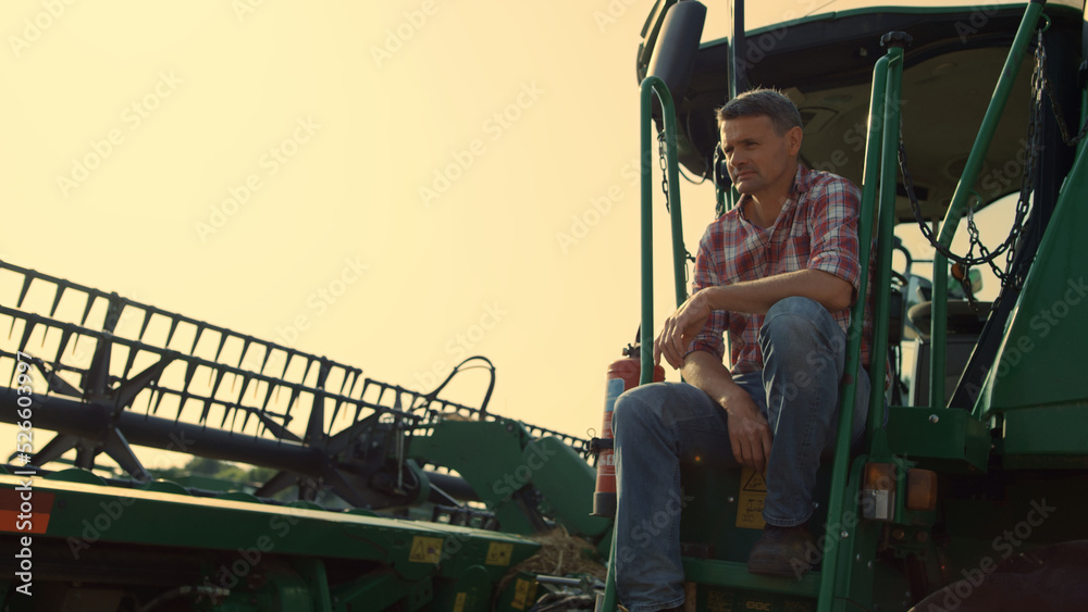 Harvester driver resting field in sunlight. Farmer inspecting cropping machinery