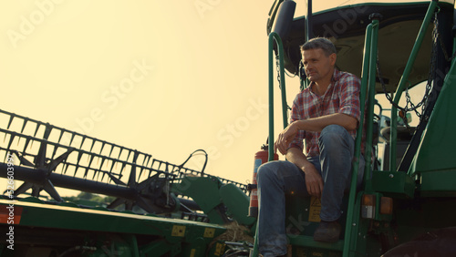 Harvester driver resting field in sunlight. Farmer inspecting cropping machinery