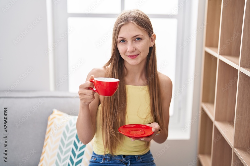 Young caucasian woman drinking coffee sitting on sofa at home Young caucasian woman drinking coffee sitting on sofa at home