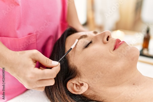 Middle age hispanic woman having eyebrows treatment at beauty center