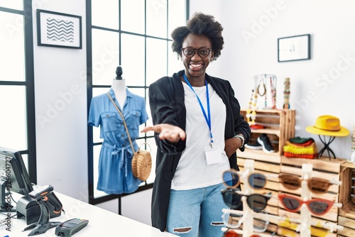 African young woman working as manager at retail boutique smiling cheerful offering palm hand giving assistance and acceptance. photo