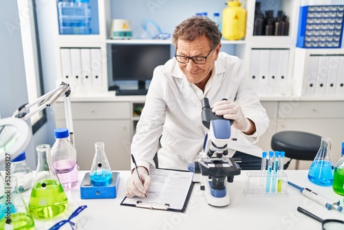 Middle age man wearing scientist uniform using microscope at laboratory