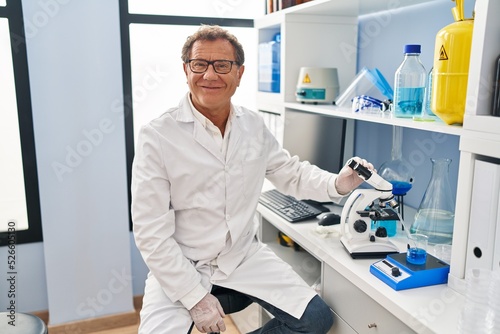 Senior man working at scientist laboratory looking positive and happy standing and smiling with a confident smile showing teeth