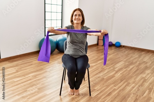 Middle age caucasian woman smiling confident training using elastic band at sport center