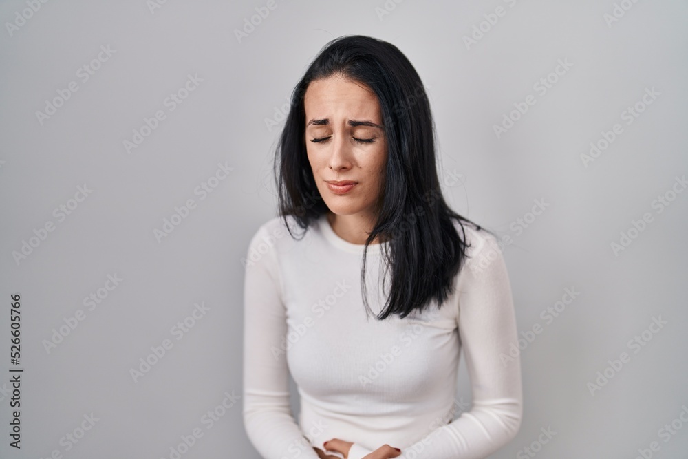 Hispanic woman standing over isolated background with hand on stomach because nausea, painful disease feeling unwell. ache concept. Hispanic woman standing over isolated background with hand on stomach because nausea, painful disease feeling unwell. ache concept.
