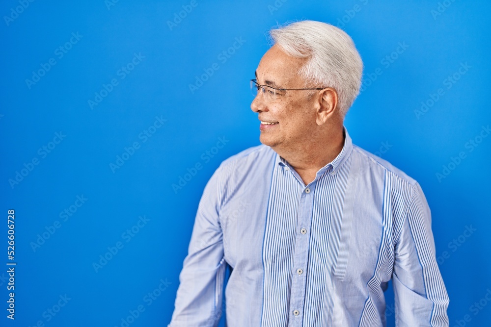 Hispanic senior man wearing glasses looking away to side with smile on face, natural expression. laughing confident.