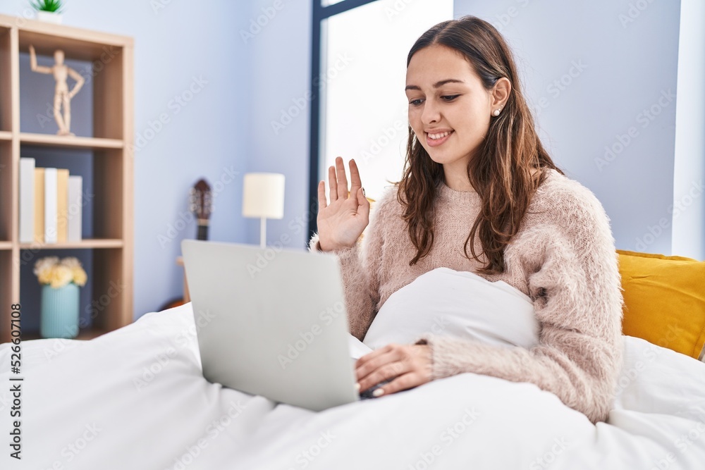 Young hispanic woman using computer laptop on the bed looking positive and happy standing and smiling with a confident smile showing teeth