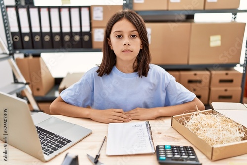 Young hispanic girl working at small business ecommerce with serious expression on face. simple and natural looking at the camera.