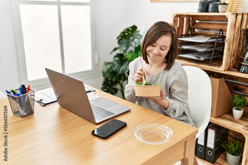 Brunette woman with down syndrome working eating salad at business office Brunette woman with down syndrome working eating salad at business office