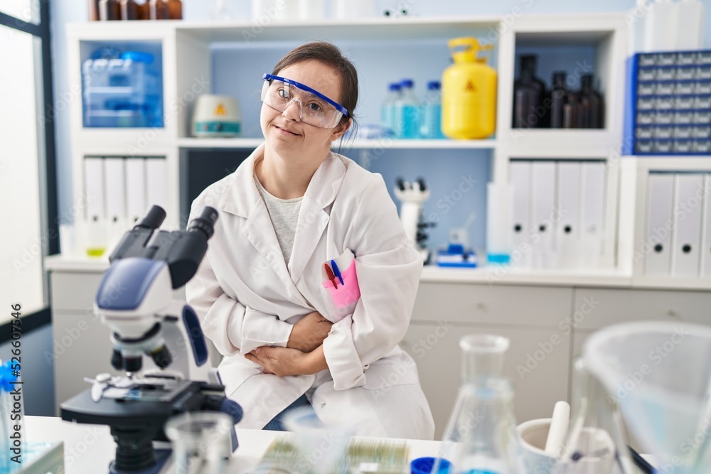 Hispanic girl with down syndrome working at scientist laboratory with hand on stomach because indigestion, painful illness feeling unwell. ache concept. Hispanic girl with down syndrome working at scientist laboratory with hand on stomach because indigestion, painful illness feeling unwell. ache concept.