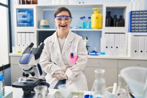 Hispanic girl with down syndrome working at scientist laboratory smiling and laughing hard out loud because funny crazy joke with hands on body.