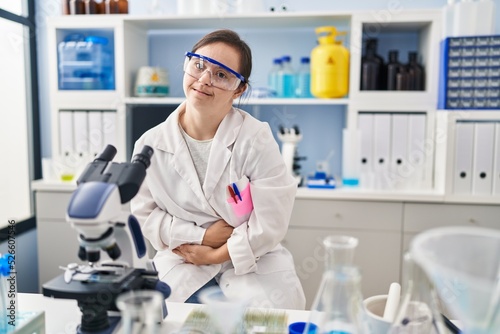 Hispanic girl with down syndrome working at scientist laboratory with hand on stomach because indigestion  painful illness feeling unwell. ache concept.