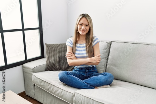 Asian young woman sitting on the sofa at home happy face smiling with crossed arms looking at the camera. positive person.