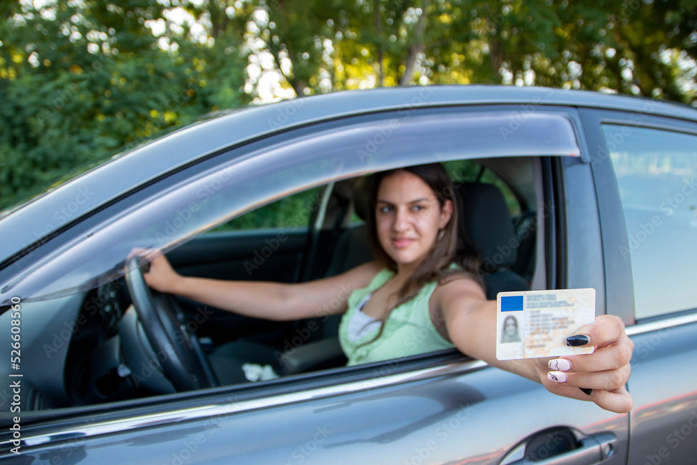 Teenager girl  showing his driver's license in the car window after passing the exam