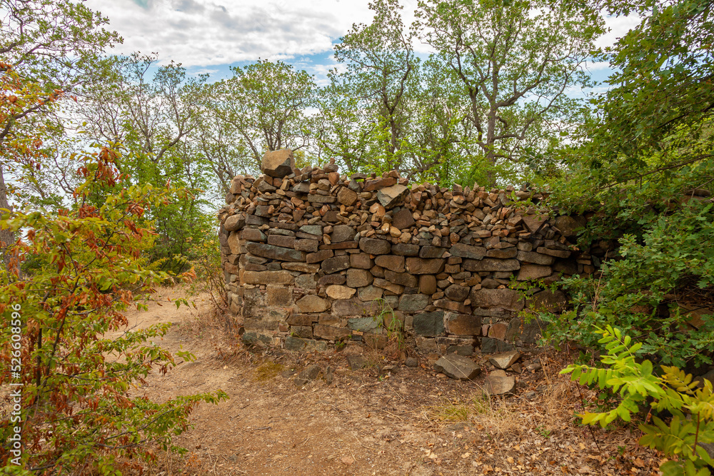 View on the stone wall of old ruined chapel on the Ayu-Dag mountain with cloudy sky and oak trees at background. Partenit, Crimea, Ukraine