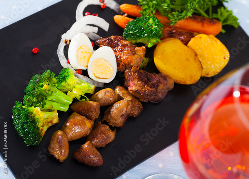 Delicious fried chicken hearts on black serving platter with baked potatoes, carrots, broccoli and greens photo