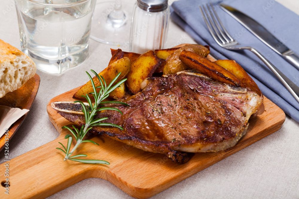 Appetizing savory veal entrecote with fried potatoes on wooden serving board..