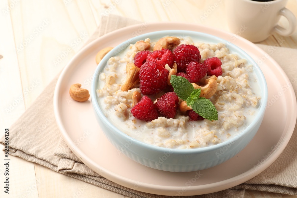 Bowl with tasty oatmeal porridge with nuts and raspberries on table, closeup. Healthy meal