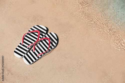 Stylish flip flops on sandy beach near sea, above view. Space for text