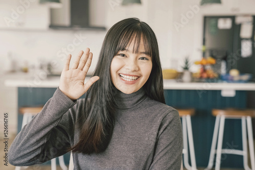 Young adult Asian woman smiling, waving and looking at camera, distance learning, online teaching, video conference concept