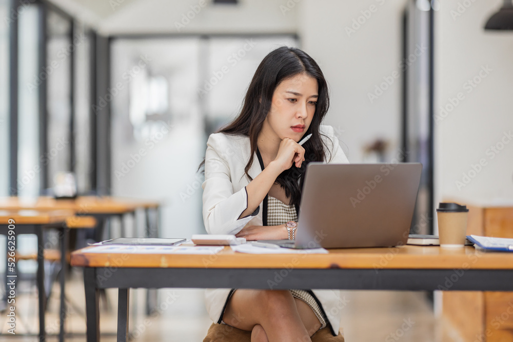 Female Business Asian working on documents on laptop in the workplace, Young asian woman sitting at table doing planning financial report, business plan investment, finance analysis concept. Female Business Asian working on documents on laptop in the workplace, Young asian woman sitting at table doing planning financial report, business plan investment, finance analysis concept.