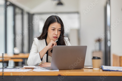 Female Business Asian working on documents on laptop in the workplace, Young asian woman sitting at table doing planning financial report, business plan investment, finance analysis concept.