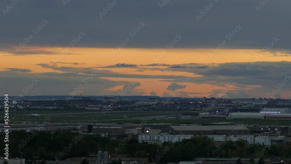 Wide shot of plane flying past large airport during dusk Wide shot of plane flying past large airport during dusk