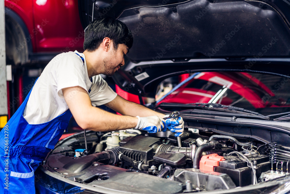 Professional car technician mechanic team in uniform work fixing vehicle car engine and maintenance repairing checking under the car hood in auto service. Automobile service garage Professional car technician mechanic team in uniform work fixing vehicle car engine and maintenance repairing checking under the car hood in auto service. Automobile service garage