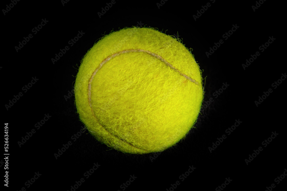 Fuzzy yellow tennis ball photographed in closeup detail against a dark background