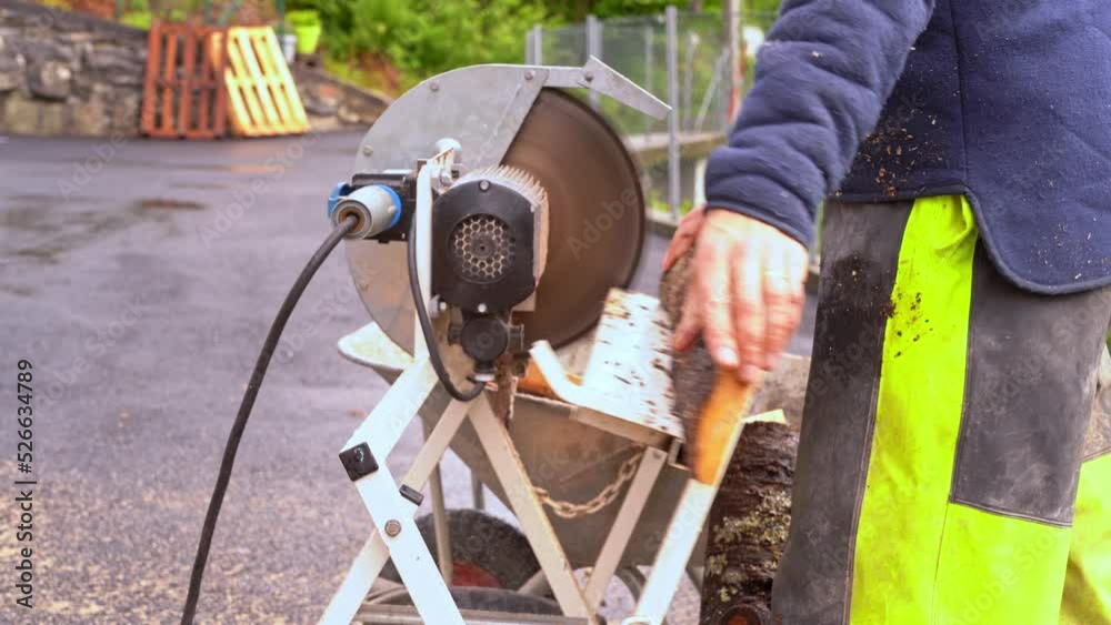 Man using crosscut saw to cut firewood from wooden pine planks - Closeup of saw and wood falling into wheelbarrow in 20 percent slow motion and blurred background Man using crosscut saw to cut firewood from wooden pine planks - Closeup of saw and wood falling into wheelbarrow in 20 percent slow motion and blurred background