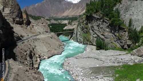 Drone shot of turquoise blue water river flowing under a bridge in Karakoram mountain range along Karakoram highway, moving through mountain pass towards bridge photo