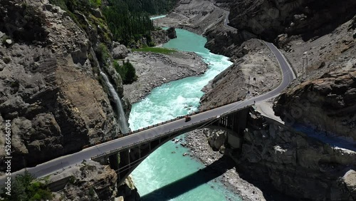 Drone shot of turquoise blue water river flowing under a bridge in Karakoram mountain range along Karakoram highway, revealing photo