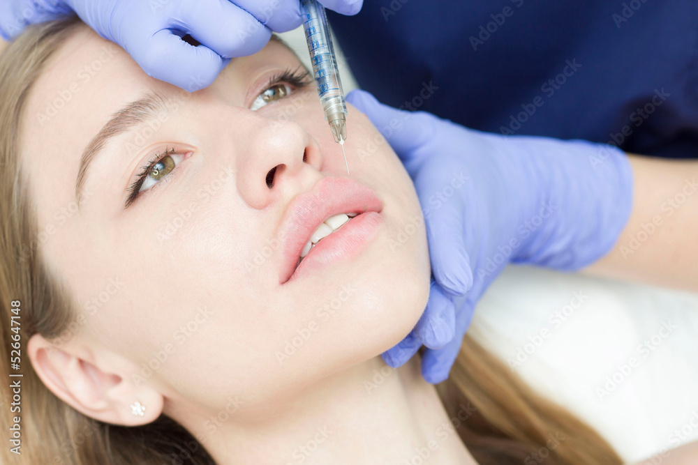A woman with beautiful clear skin. A cosmetologist makes injections to increase the lips and anti-wrinkles of a beautiful woman. Women's cosmetology in a beauty salon. Lip augmentation A woman with beautiful clear skin. A cosmetologist makes injections to increase the lips and anti-wrinkles of a beautiful woman. Women's cosmetology in a beauty salon. Lip augmentation