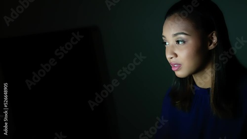 Young Black woman looking screen in dark room. photo