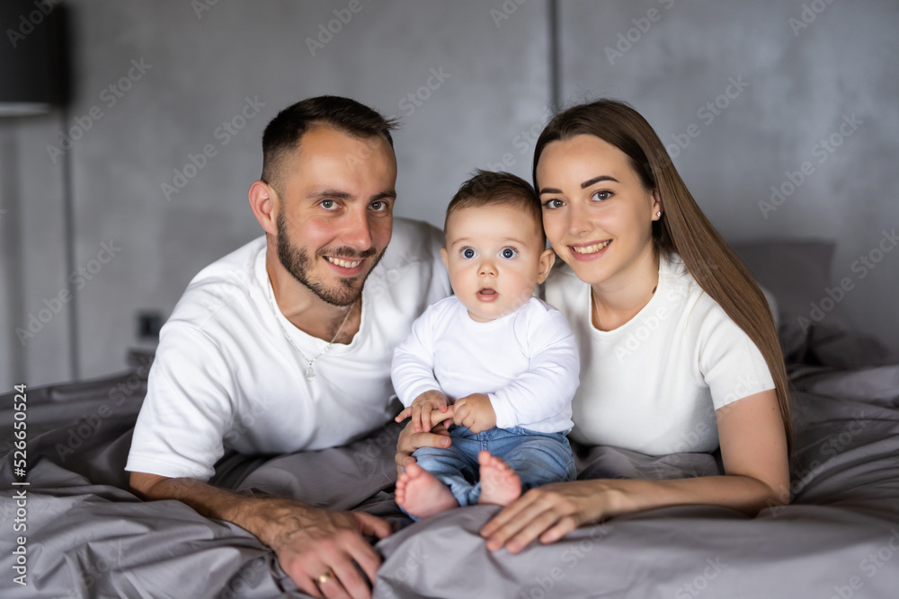 Happy parenthood. Cheerful mom and dad embracing with cute baby in bed