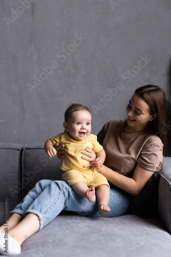 Mother and baby laugh together at home. They are sitting on the sofe in a brightly lit living room at the weekend together.