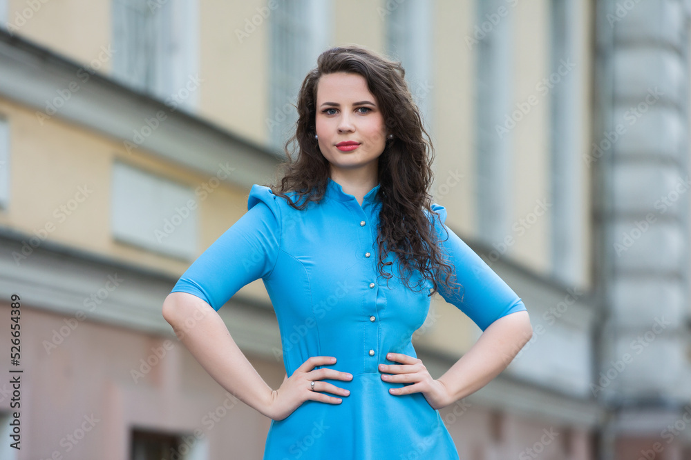 Portrait of a beautiful white European brunette girl wearing a blue dress on the street in the summer