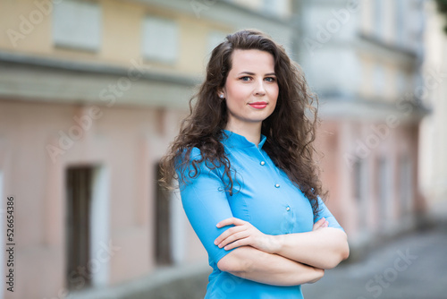 Portrait of a beautiful white European brunette girl wearing a blue dress on the street in the summer