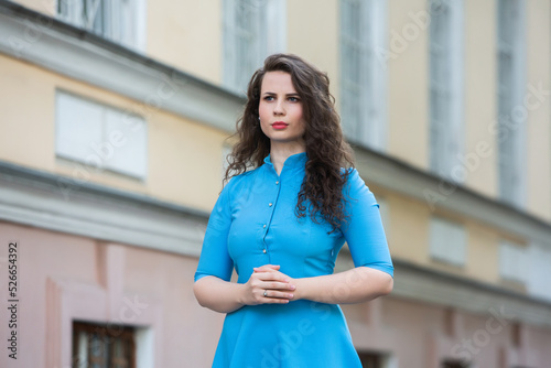 Portrait of a beautiful white European brunette girl wearing a blue dress on the street in the summer